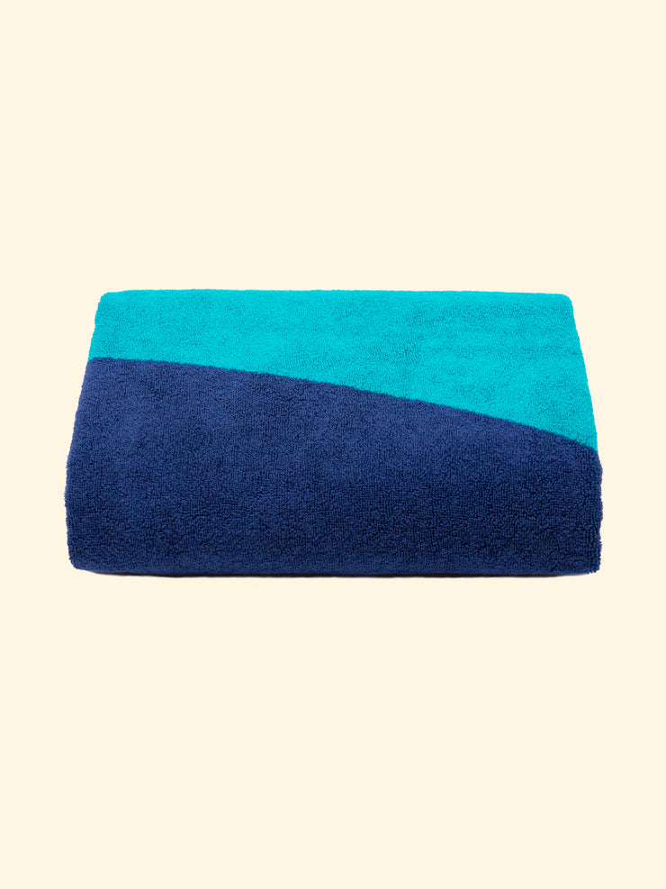 Modelo "Swell" de Tucca toalla de playa 100% algodón orgánico, perfectamente doblada como se presenta en el embalaje, con dos alfileres en cada lado, los que se pueden utilizar para fijar su toalla de playa a la arena.