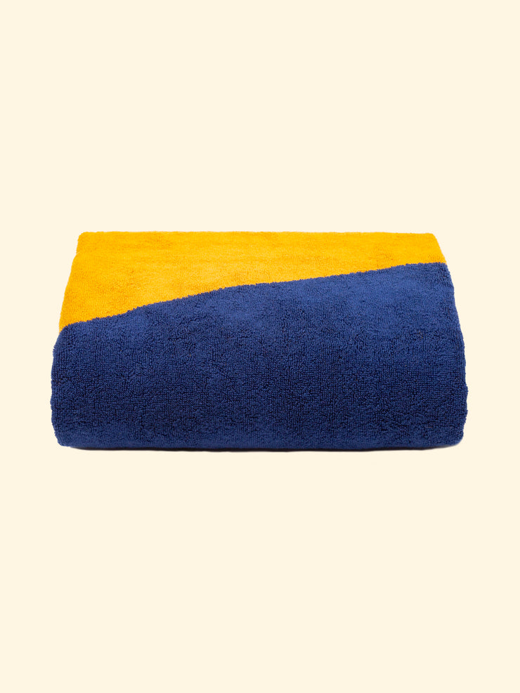 Modelo "Duna" de Tucca toalla de playa 100% algodón orgánico, perfectamente doblada tal y como se presenta en el embalaje, con dos alfileres en cada lado, los que se pueden utilizar para fijar su toalla de playa a la arena.