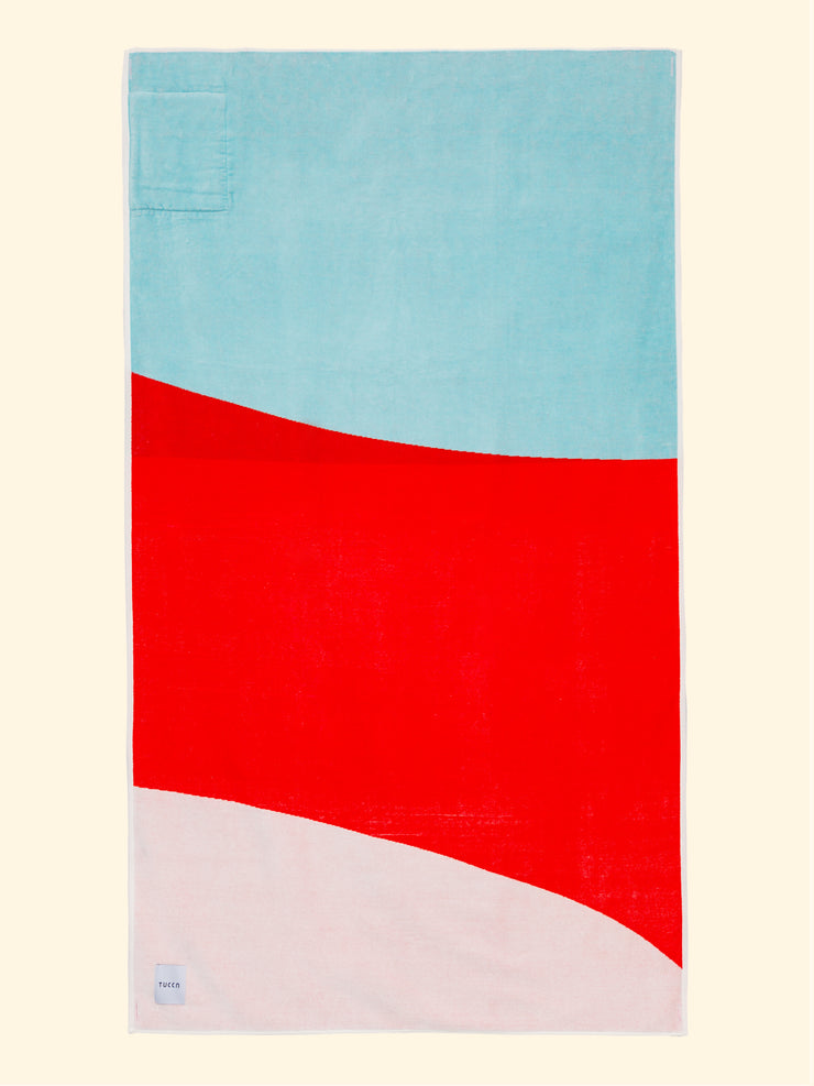 Tucca "Berry" beach towel extended. Light blue, red and white colors in big blocks composing a beautiful design. Large beach towel that doesn't get blown by the wind. Super soft texture as it is made with 100% organic cotton.