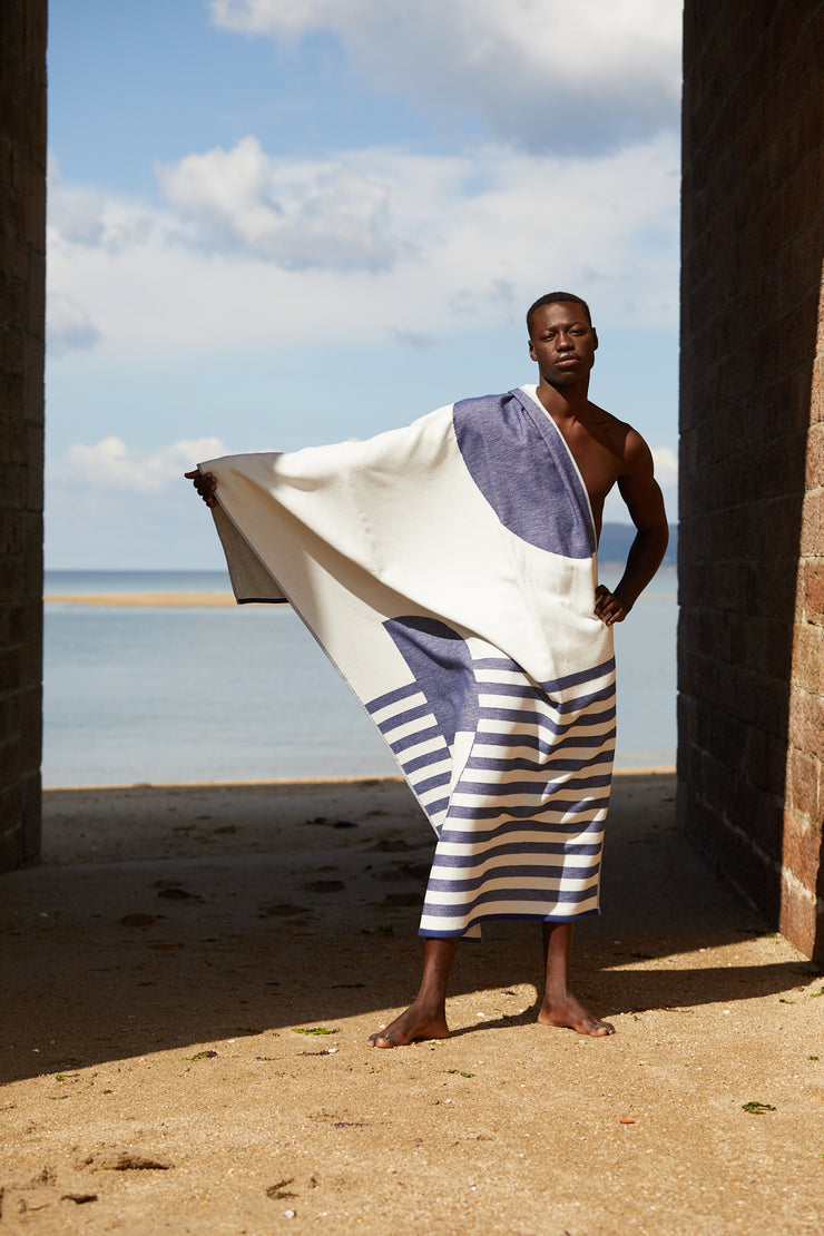Model drying himself under a bridge in the beach with the Tucca "Florida" style. An extra light beach towel that doesn't get blown by the wind. Super soft texture as it is made with 100% organic cotton.