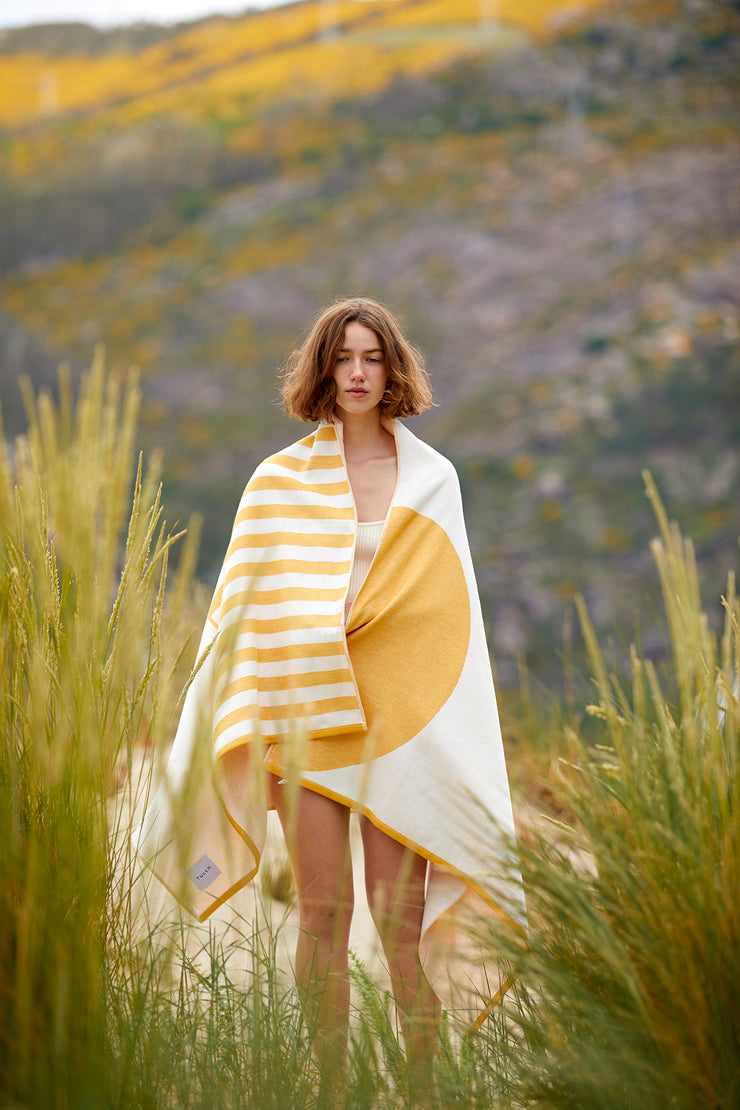 Chica cubriéndose con la Tucca estilo "Danai". Una toalla de playa extra ligera que no se la lleva el viento. Textura súper suave al estar confeccionada con algodón 100% orgánico.
