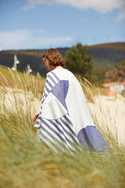 Chica caminando por los alrededores de la playa sosteniendo una Tucca estilo "Florida". Una toalla de playa extra ligera que no se la lleva el viento. Textura súper suave al estar fabricada con algodón 100% orgánico.
