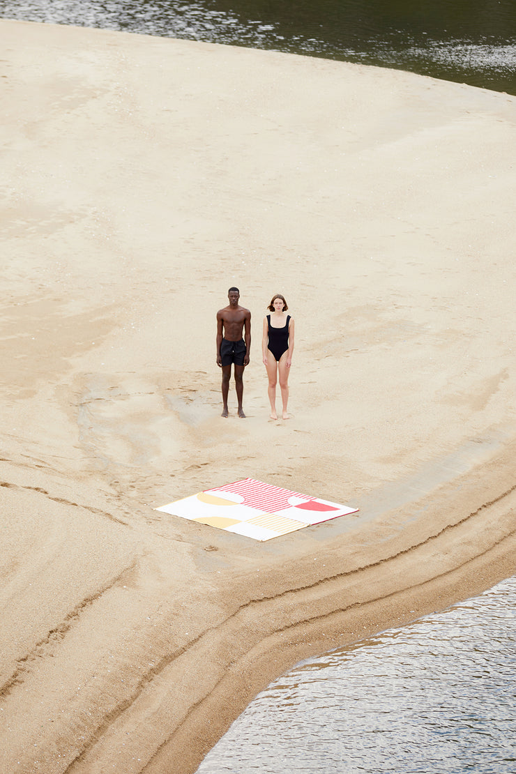 Dos toallas de playa conectadas entre sí. Las imágenes muestran los diseños conectables de las toallas de playa Danai y Crassha premium ligh. Una pareja disfrutando de la playa juntos con sus toallas de playa conectadas entre sí.
